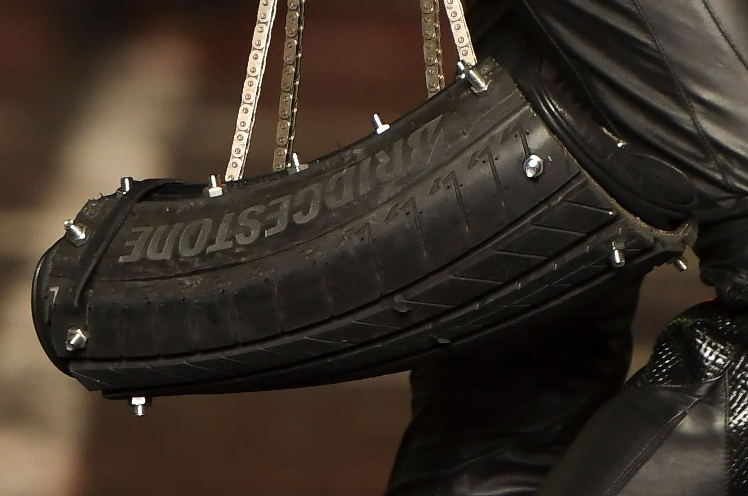 A bolsa de pneu do look 6 da Forca X, da FORCA Studio, na SPFW N61: trecho de pneu Bridgestone curvado, com o nome em relevo no flanco, parafusos cromados e alças de corrente de bicicleta. Foto: Zé Takahashi